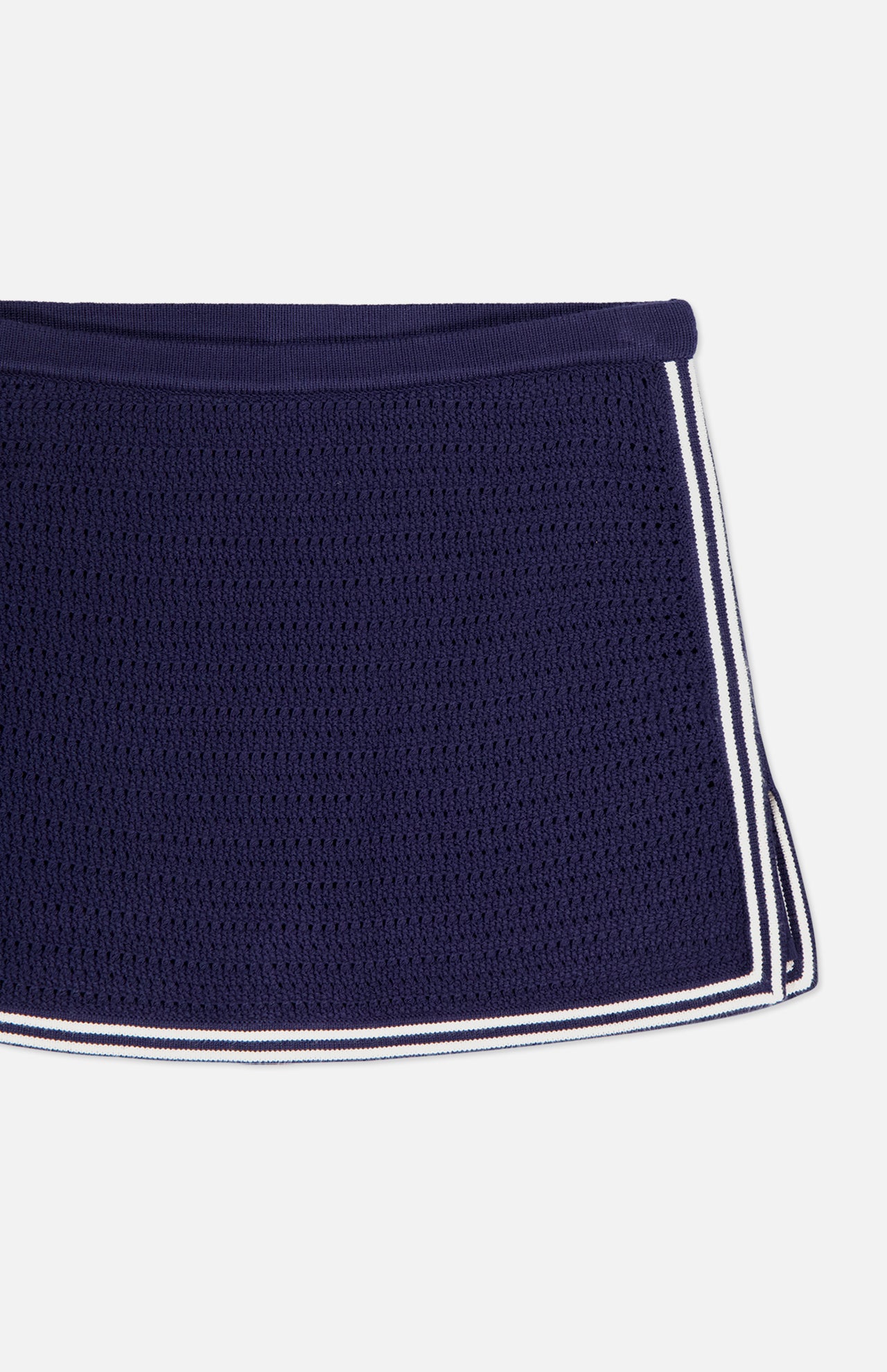 A close-up of the Monique Knit Mini Skort by AMANDA UPRICHARD, featuring a fitted navy silhouette with mesh texture and white double stripes along the hem, displayed on a white background.