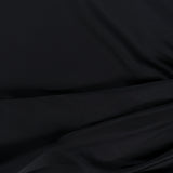 A close-up of smooth, black fabric with gentle folds and soft shadows creates a subtle texture and sense of depth—perfect for the Olandria Waist Bustle Mini Dress by AMANDA UPRICHARD.