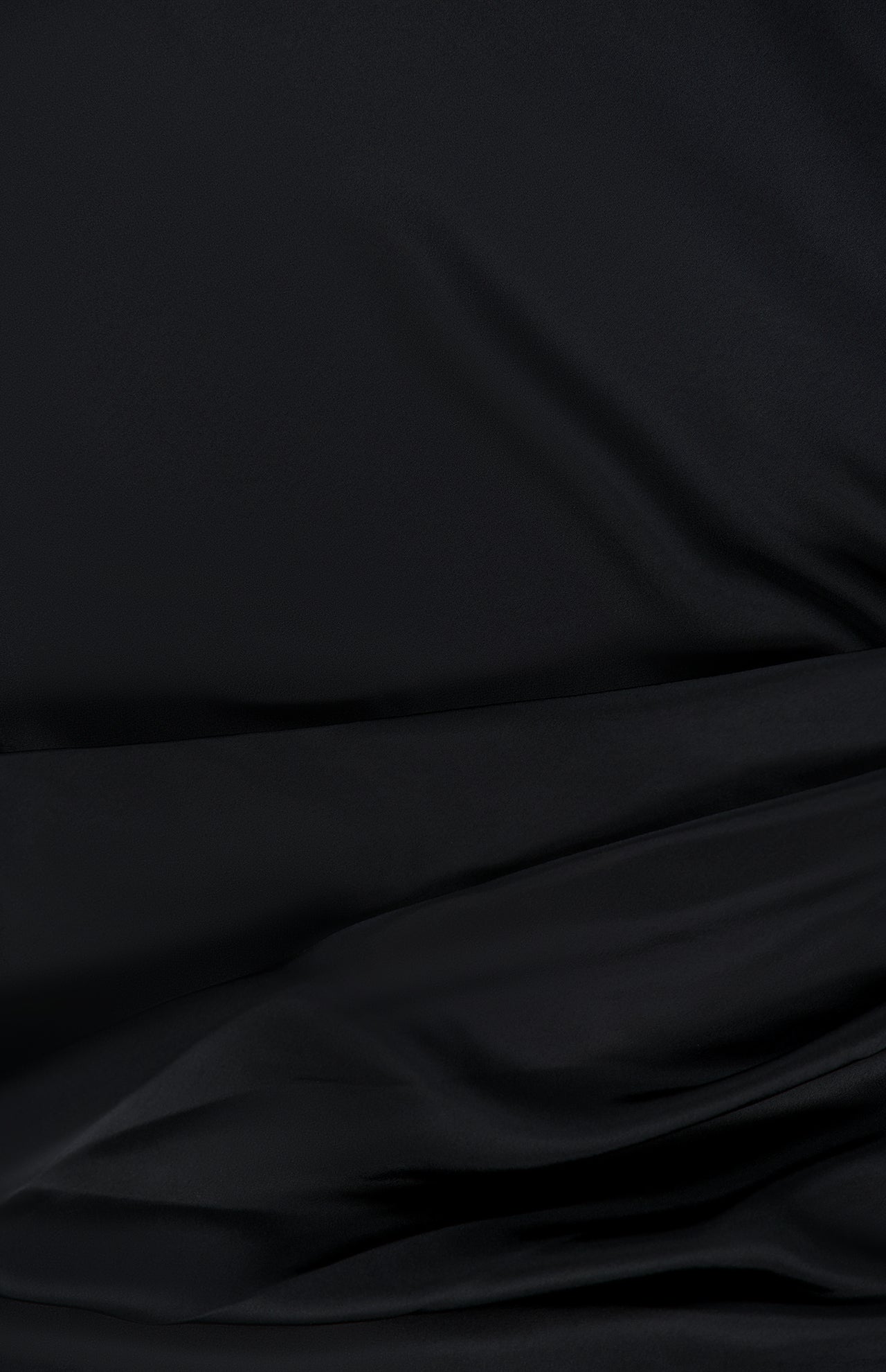 A close-up of smooth, black fabric with gentle folds and soft shadows creates a subtle texture and sense of depth—perfect for the Olandria Waist Bustle Mini Dress by AMANDA UPRICHARD.