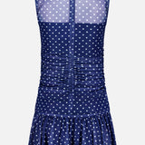 The Rumi Sleeveless Polka Dot Dress by AMANDA UPRICHARD features a navy blue mini silhouette with white polka dots, sheer high-neck bodice, ruching at the waist, back zipper, and a flared ruffled hem—perfect for a chic statement.