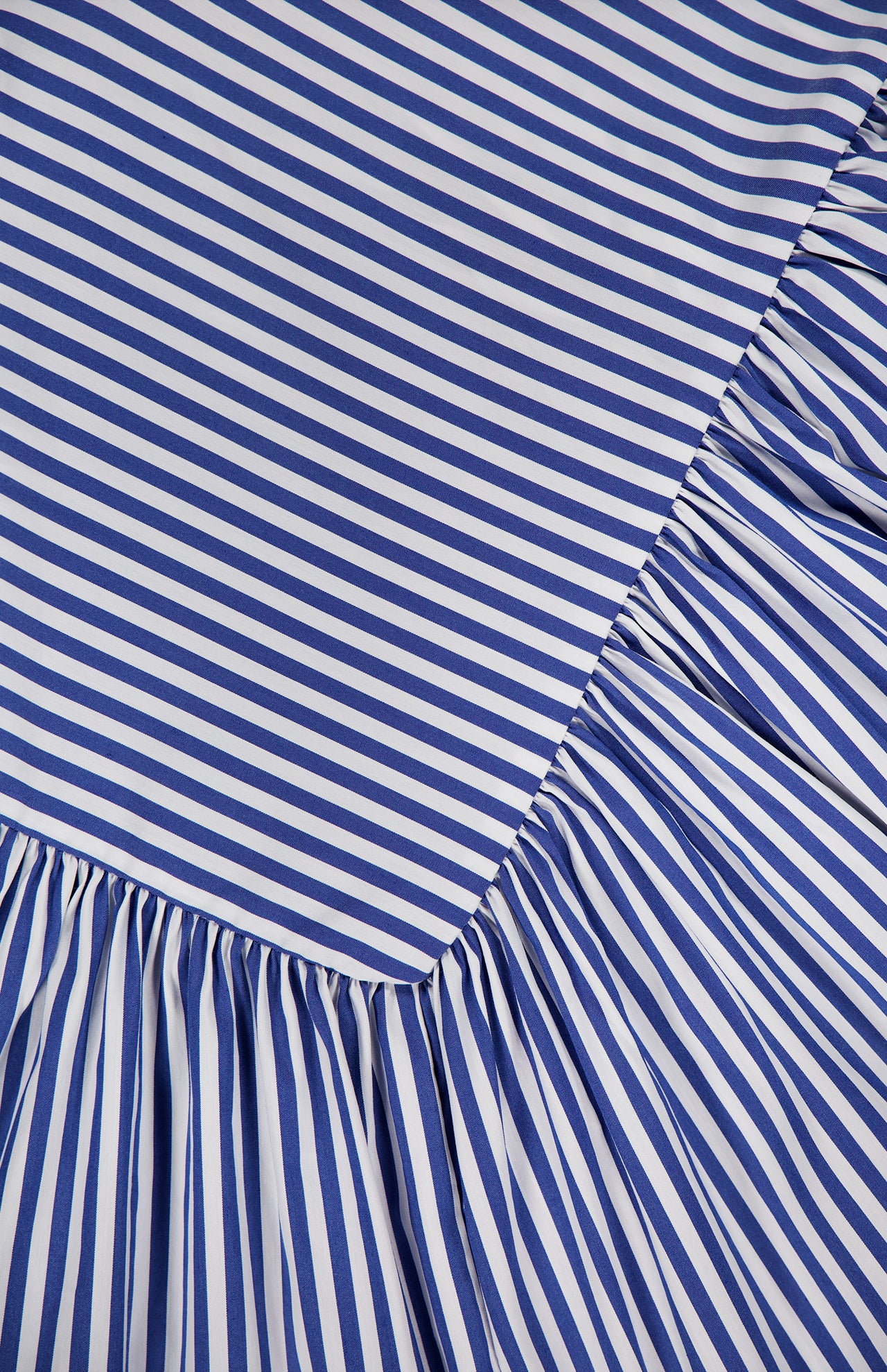 Close-up of blue and white diagonal stripes on the Spencer Striped Midi Dress by AMANDA UPRICHARD, featuring an angled seam and gathered, ruffled fabric below—perfect for a summer party look.