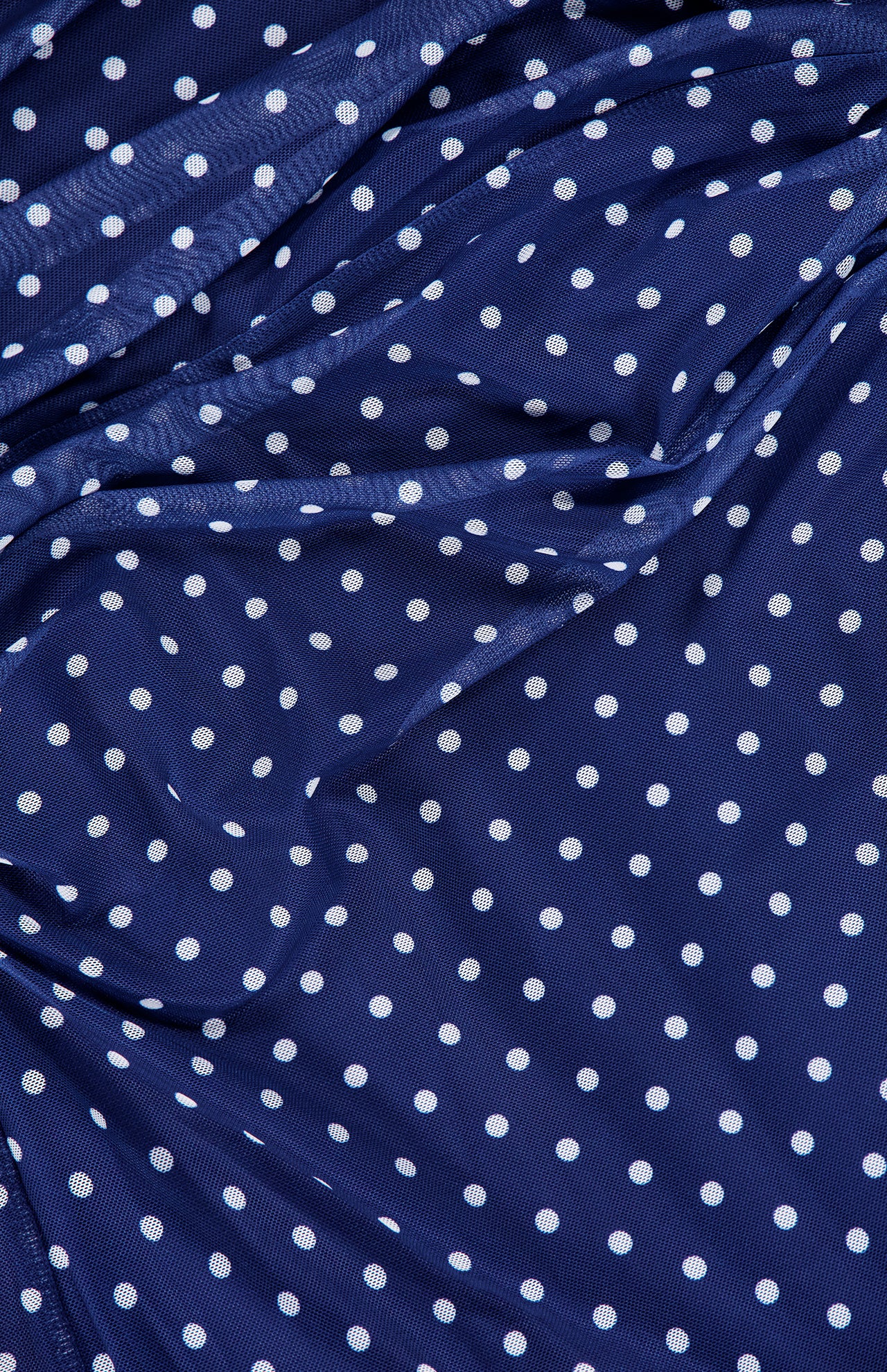 The Zoey Polka Dot Midi Dress by AMANDA UPRICHARD features dark blue fabric with evenly spaced white polka dots, draping in soft, uneven folds for a timeless and classic look.