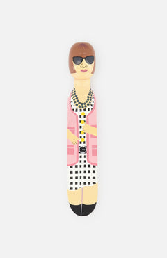 The WEDGIE ‘Ana’ Wood Door Stopper features a hand-painted woman with a bob haircut, black sunglasses, pink jacket, checkered dress, and beaded necklace—adding designer flair to your space.