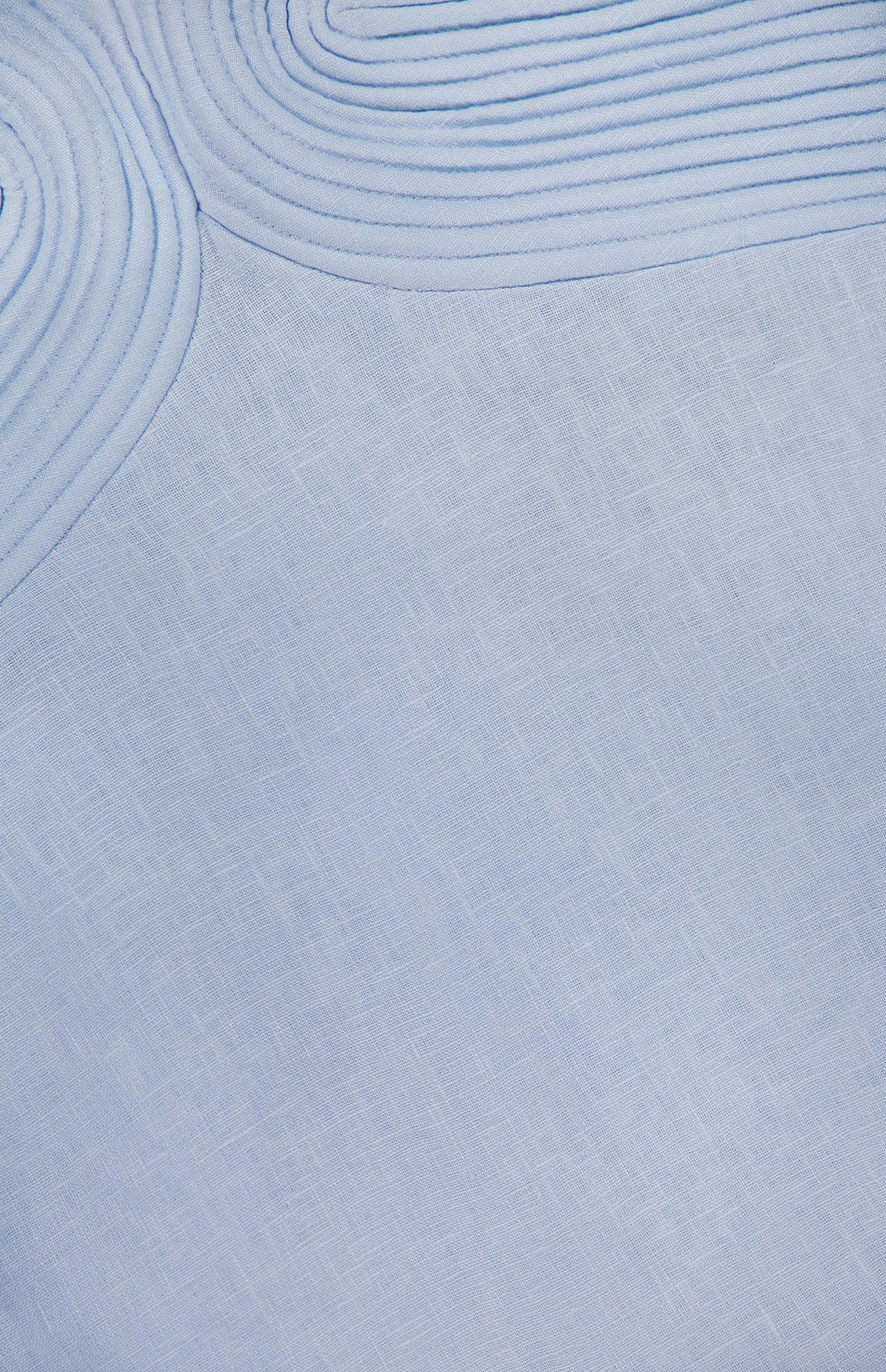 Close-up of ANDRÉS OTÁLORA's Amari Ama Linen Mini Dress in baby blue, showing smooth linen fabric with a subtle crosshatch pattern and raised, concentric stitched lines curving at the top left.