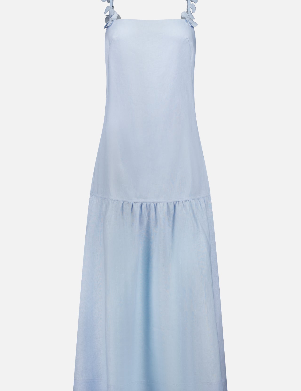 The Benditas Maxi Linen Dress by ANDRÉS OTÁLORA is a Mediterranean-inspired, sleeveless light blue dress with wide shoulder straps, decorative bows, and a drop waist. This knee-length baby blue dress is shown against a plain white background.