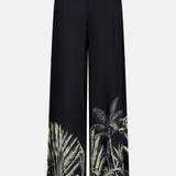 The ANDRÉS OTÁLORA En Calma Palm Print Pants are midnight navy, wide-leg pull-on pants with a high waist and green palm print accents along the lower legs for a tropical touch.