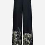 ANDRÉS OTÁLORA's En Calma Palm Print Pants are wide-leg black pull-on pants with a high waist and a green tropical palm print accenting the lower legs.