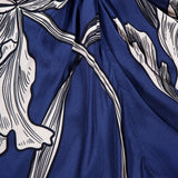 A close-up of blue fabric from the Olanna Twist Front Maxi Dress by ANDRÉS OTÁLORA, showcasing a Mediterranean-inspired white and black botanical print with stylized leaves and flowing, bold lines.