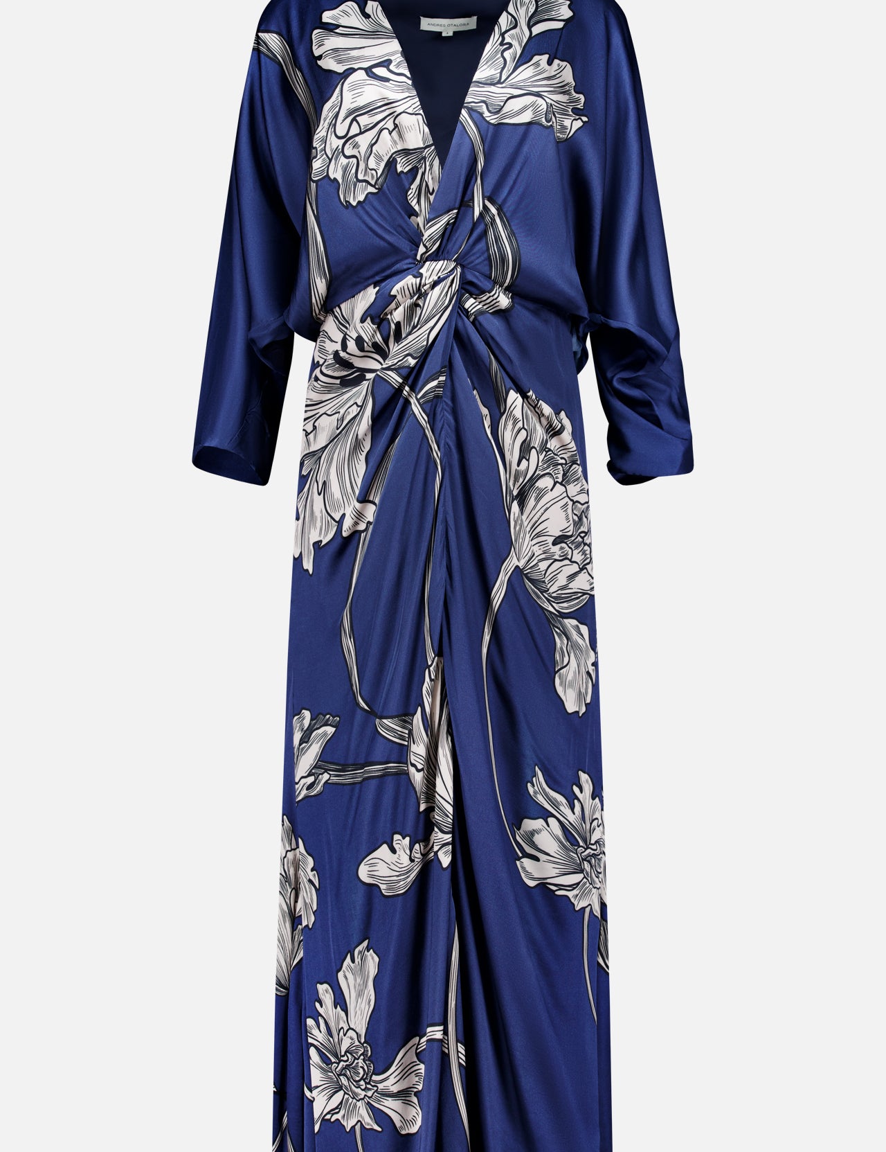 The Olanna Twist Front Maxi Dress by ANDRÉS OTÁLORA is a deep blue satin, long-sleeved dress with a knot front, draped V-neckline, and large light floral print. This Mediterranean-inspired style has a relaxed fit and falls below the knee.