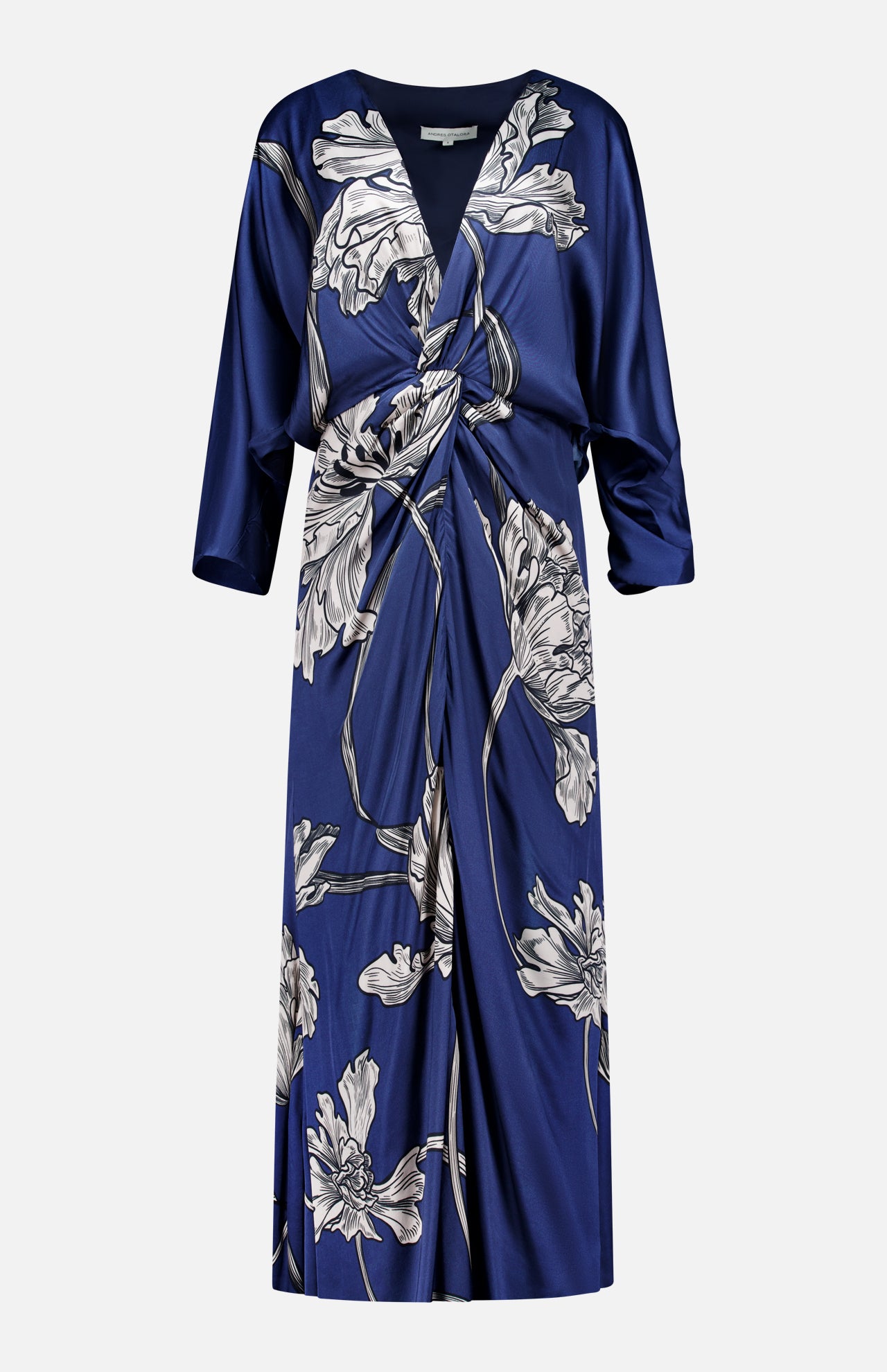 The Olanna Twist Front Maxi Dress by ANDRÉS OTÁLORA is a deep blue satin, long-sleeved dress with a knot front, draped V-neckline, and large light floral print. This Mediterranean-inspired style has a relaxed fit and falls below the knee.