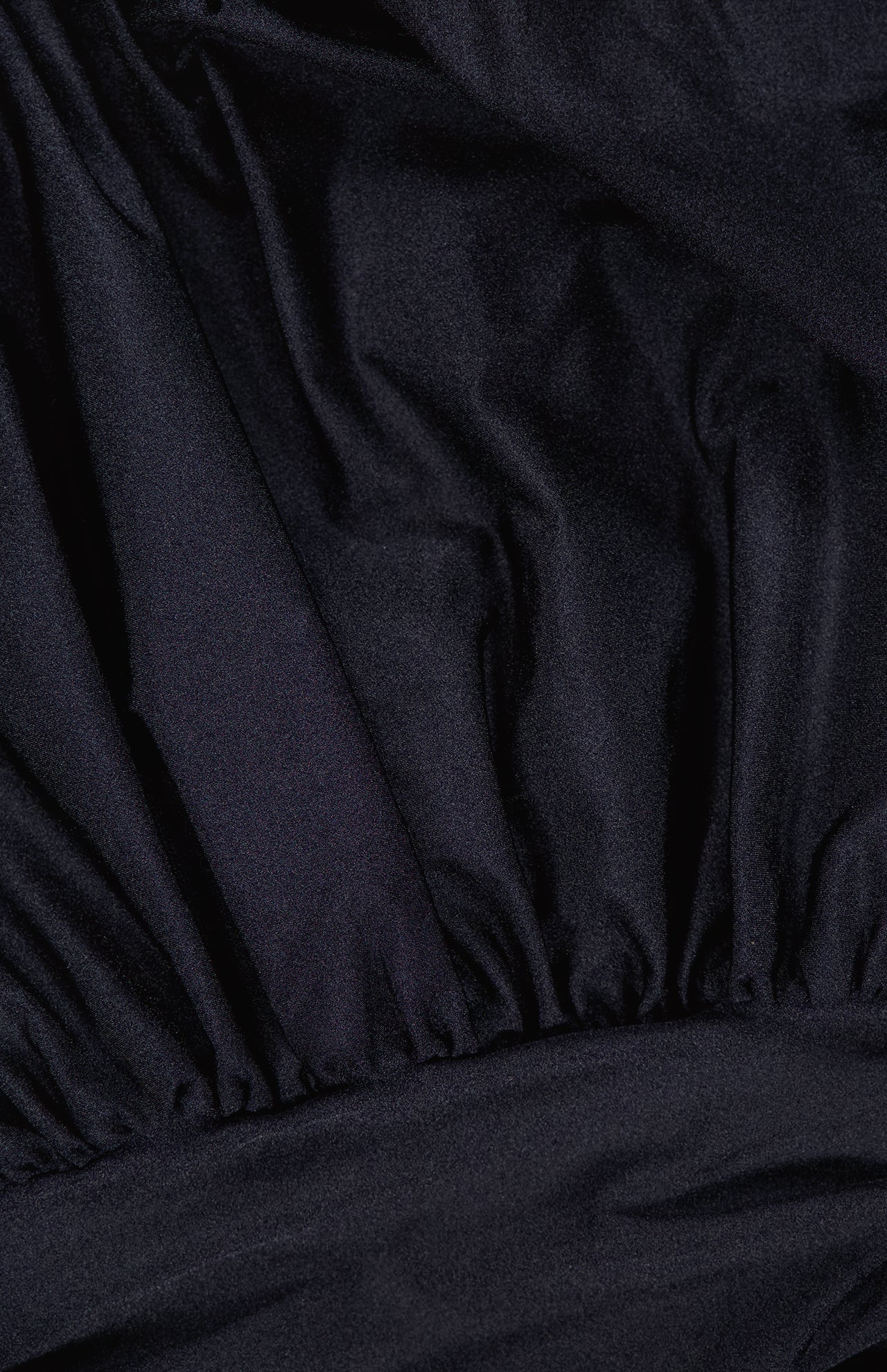 Close-up of the Tan Lejos Top by ANDRÉS OTÁLORA, featuring sculptural black fabric with gathered details, visible folds and pleats for a textured, slightly shiny finish.