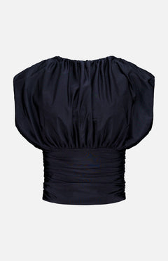 The Tan Lejos Top by ANDRÉS OTÁLORA is a sculptural black short-sleeved blouse with ruching, a wide gathered neckline, and fitted pleated waistband—an elegant going-out top shown on a plain white background.