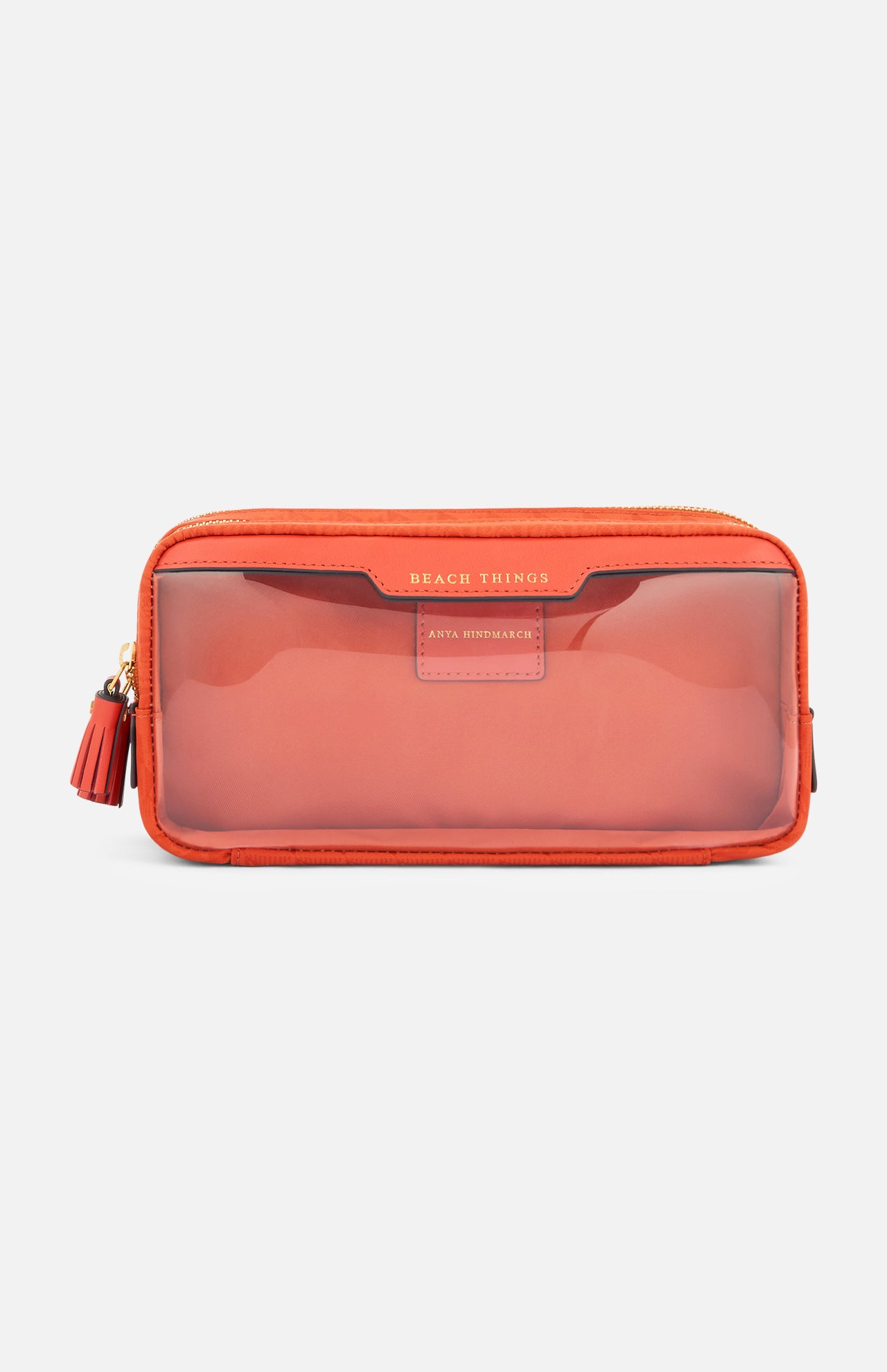 Anya Hindmarch Beach Things Pouch, a rectangular orange zippered travel case with a transparent front panel, embossed text at the top, and a small tassel on the side.