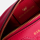 Close-up view of the interior of a dark pink Anya Hindmarch Logo Girlie Stuff Pouch, featuring a rectangular leather patch embossed with a gold bow logo and brand name.