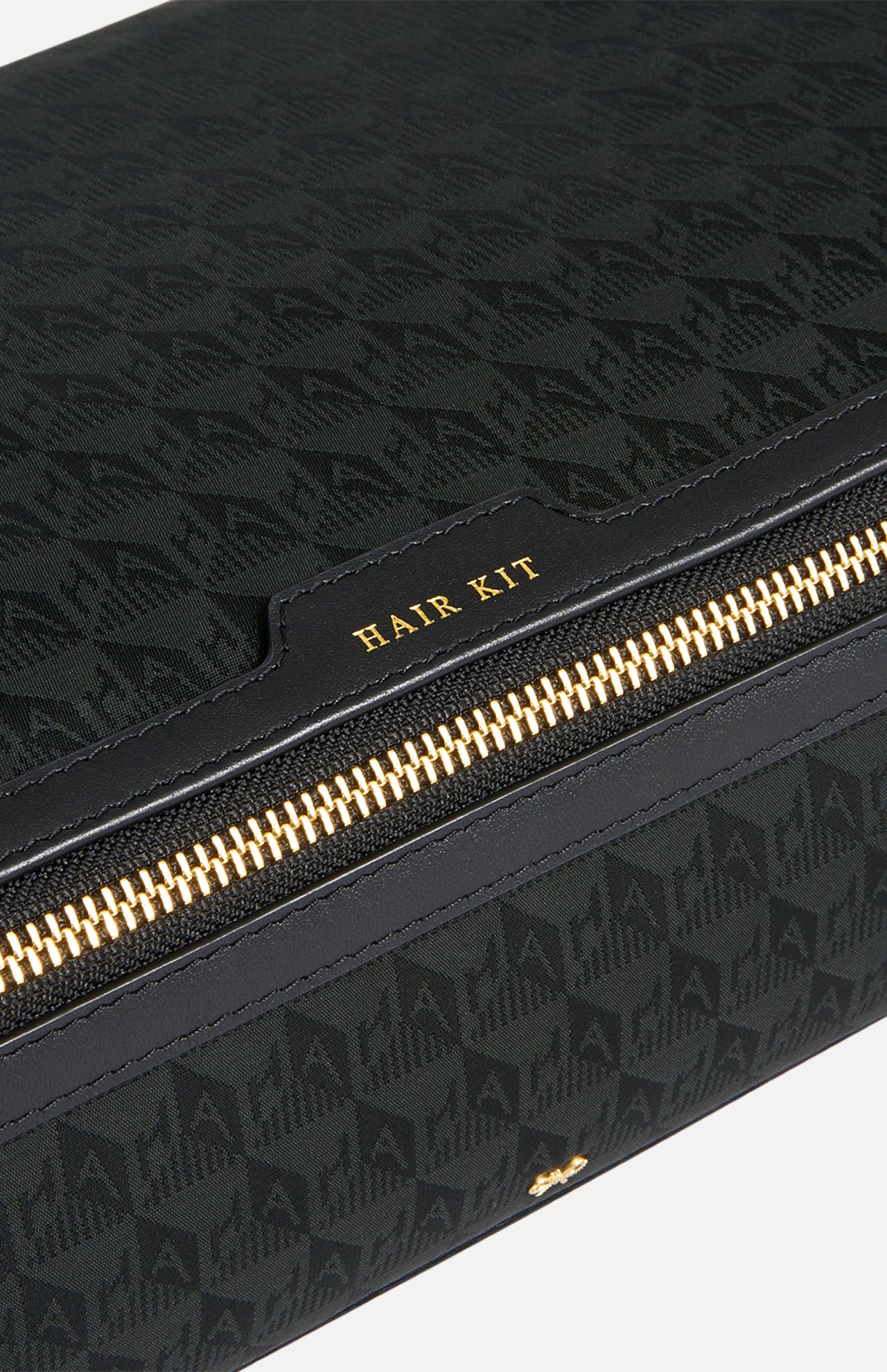 Anya Hindmarch Logo Hair Kit Travel Pouch in black with a repeating pattern and a zippered closure labeled HAIR KIT in gold lettering.