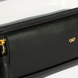 Anya Hindmarch Logo In-Flight Case in black with a zippered closure, clear plastic top, and small gold bow emblem.