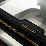 Clear, rectangular Anya Hindmarch Logo In-Flight Case with black leather trim, a gold-tone zip closure, and the word TAKE-OFF embossed in gold on the front.