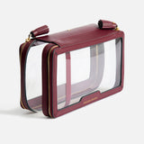 Anya Hindmarch Logo In-Flight Case in clear rectangular plastic with burgundy leather trim, gold-tone zippers, and the word TOUCH-DOWN embossed in gold on the front.