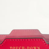 Fuchsia-colored rectangular Anya Hindmarch Logo In-Flight Case with the word TOUCH-DOWN embossed in gold lettering on the front flap.