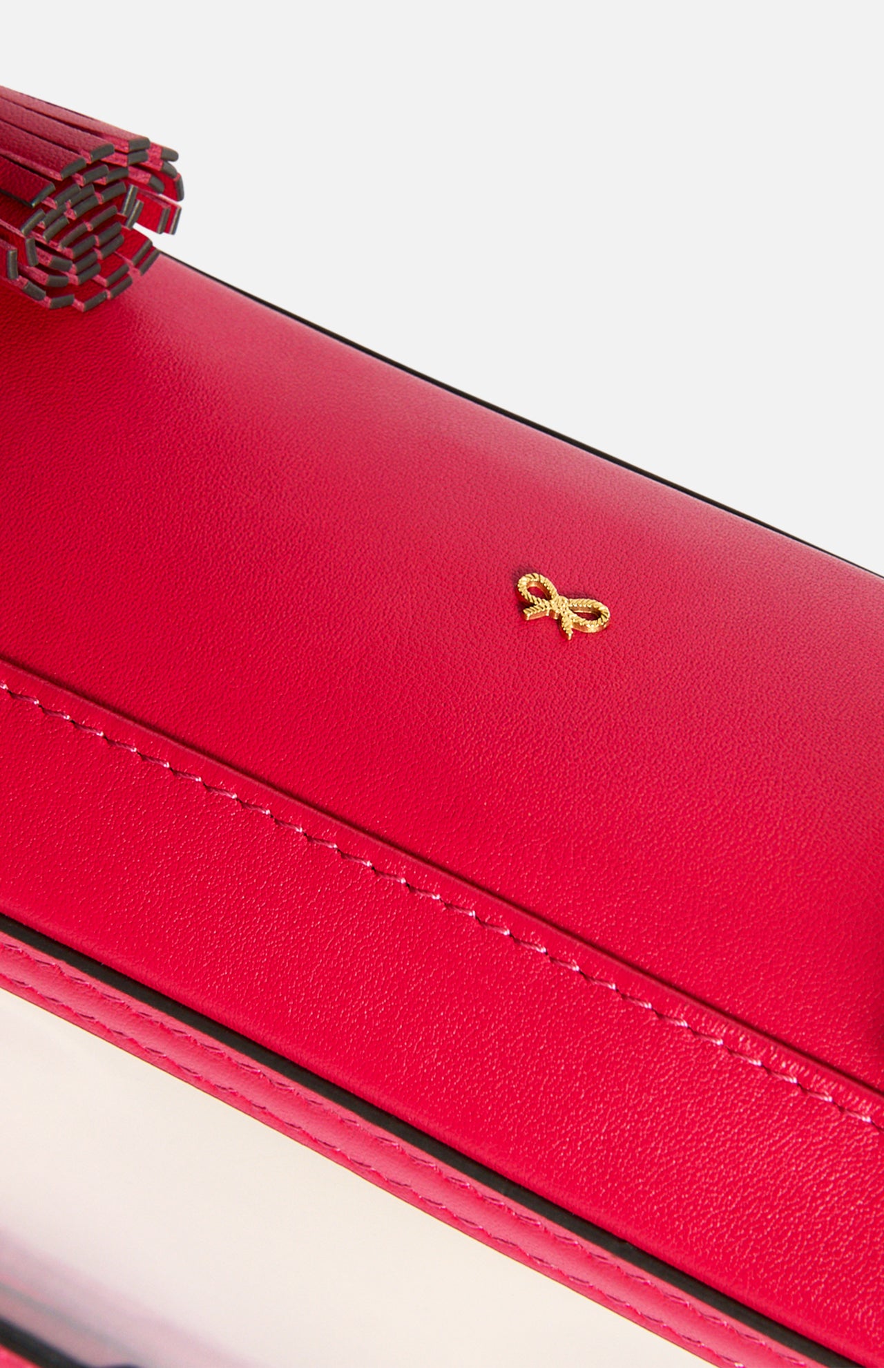 Close-up of a bright pink Anya Hindmarch Logo In-Flight Case featuring a gold bow emblem and a tassel zipper pull.