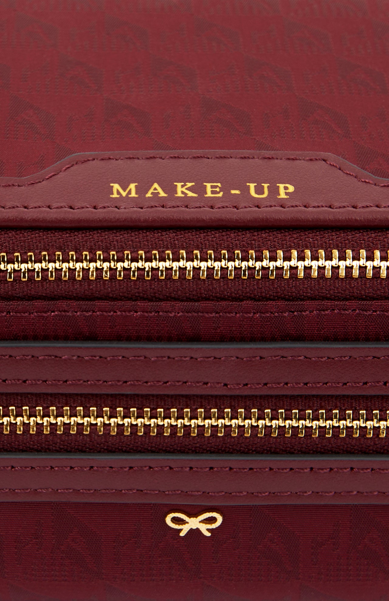 Close-up of a deep red, Italian-made Anya Hindmarch Logo Make-Up Pouch with gold zippers and the word MAKE-UP embossed on a leather tab.