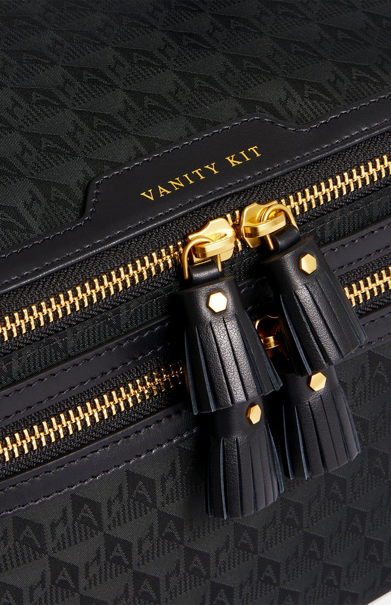 Black Anya Hindmarch Logo Vanity Kit featuring gold-tone hardware, two tassel zipper pulls, and the text VANITY KIT embossed above the main compartment of this luxury toiletry bag.