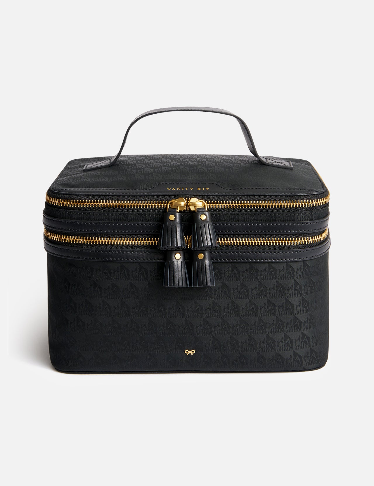 Black Anya Hindmarch Logo Vanity Kit with a top handle, a double-zippered closure with two leather tassels, and a gold-tone bow emblem on the front.