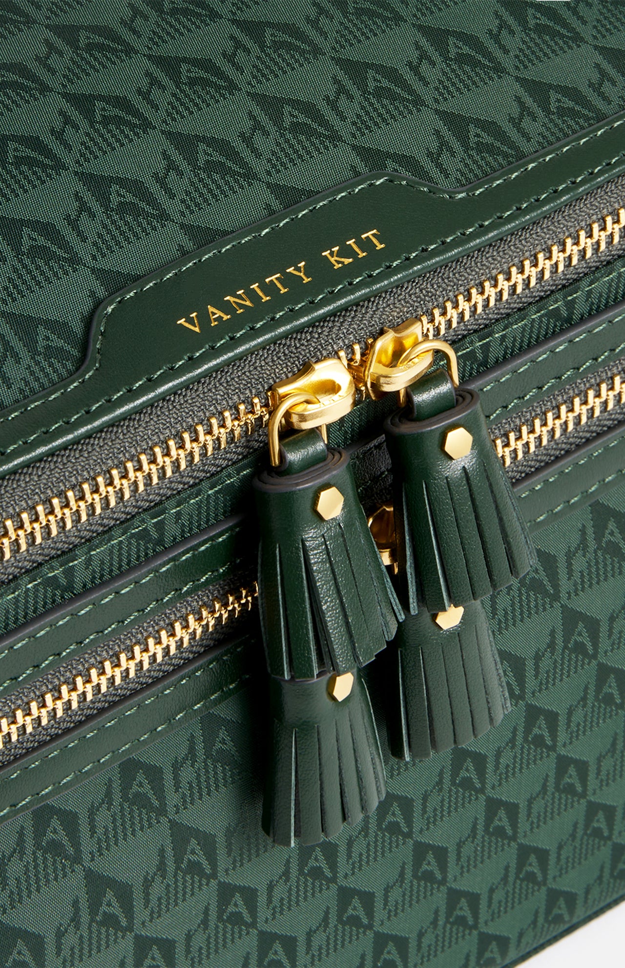 Anya Hindmarch Logo Vanity Kit in dark green with a repeating monogram pattern, gold-tone zipper pulls with tassels, and the words VANITY KIT embossed in gold.