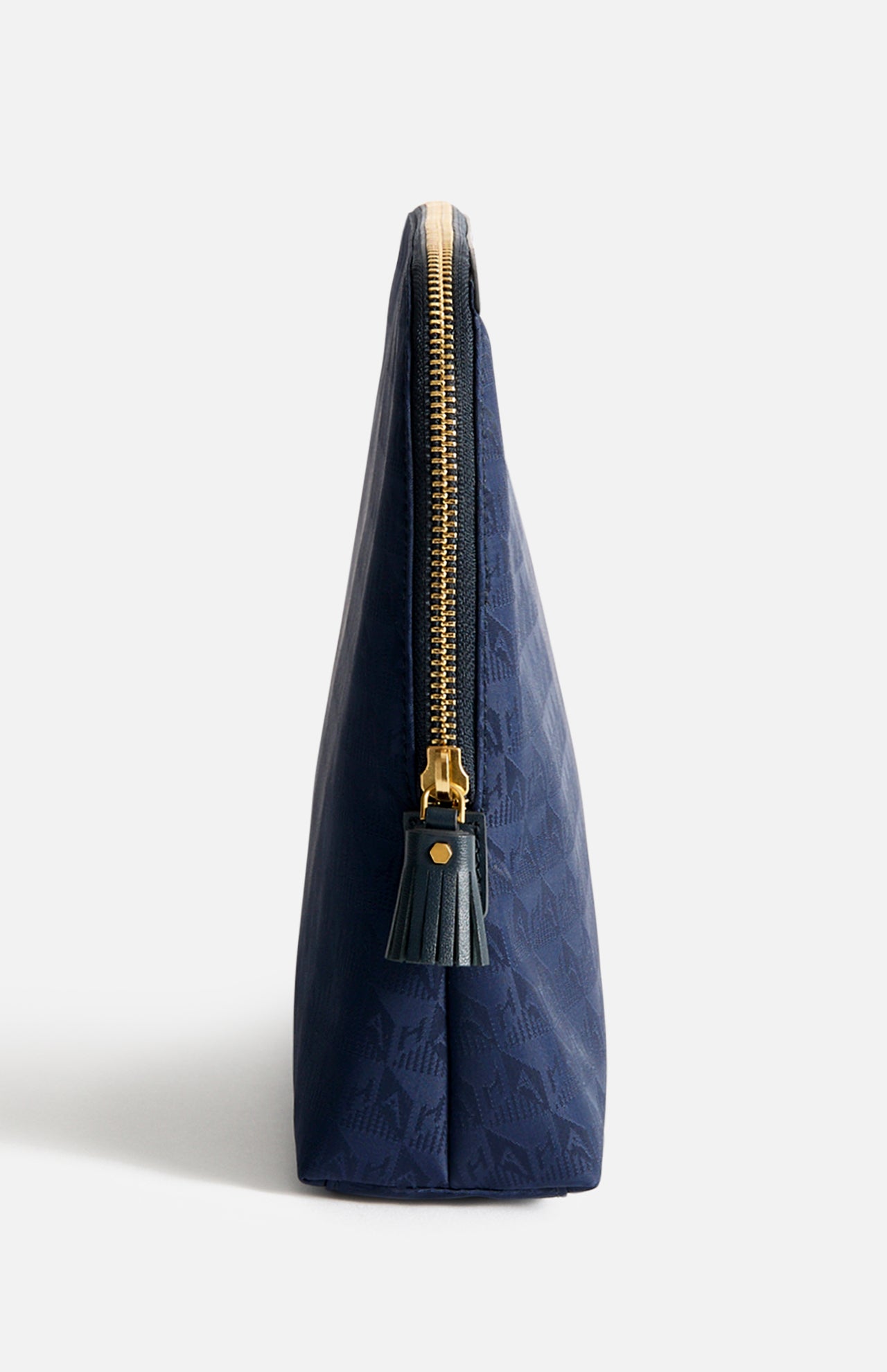 Side view of an Anya Hindmarch Lotions and Potions Pouch, a dark blue, Italian-made triangular travel pouch with a gold zipper and a matching tassel pull.