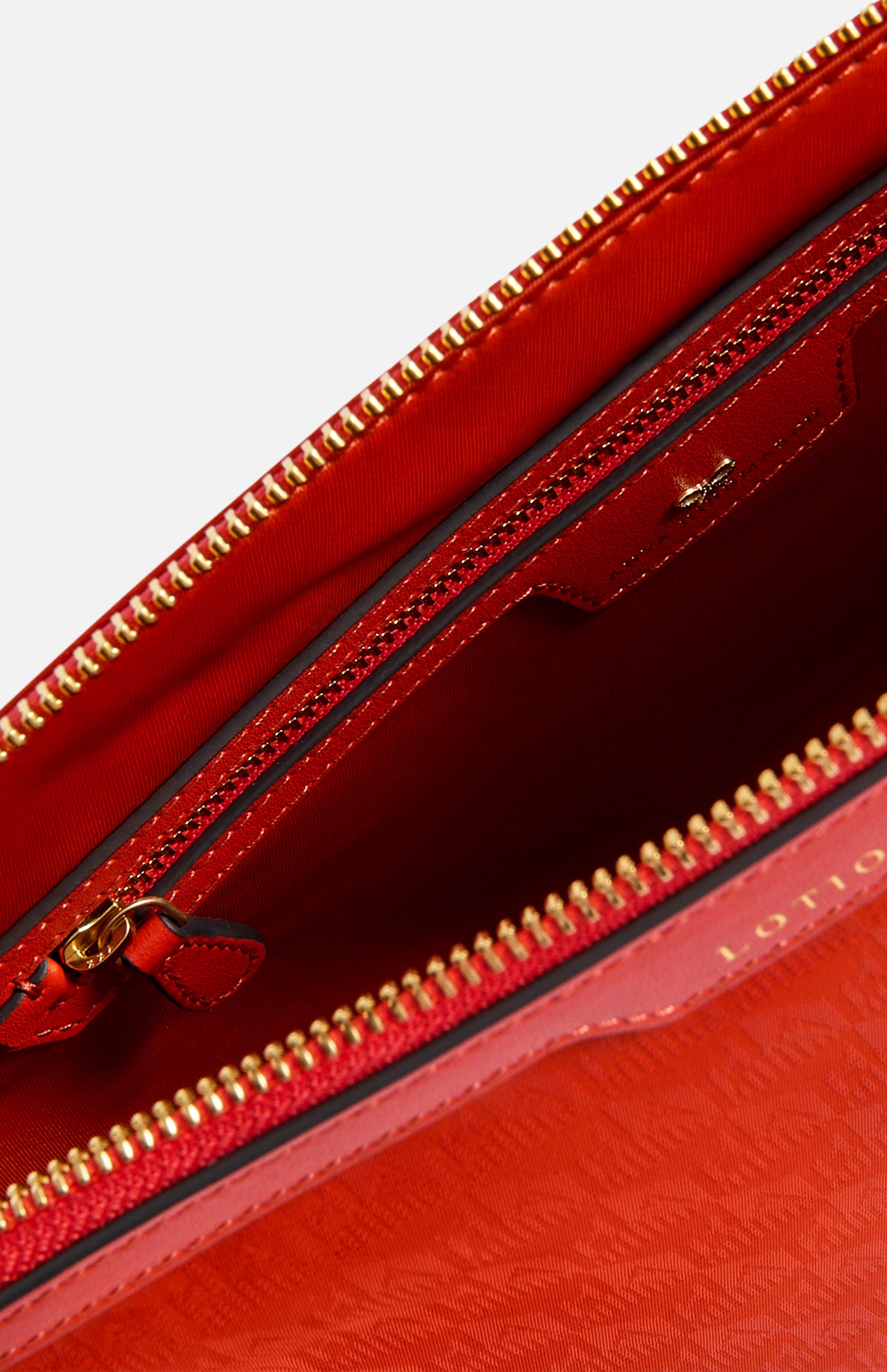 The interior of a red, Italian-made Anya Hindmarch Lotions and Potions Pouch, featuring a main compartment and an additional internal zippered pocket.