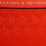 Close-up of a bright orange Anya Hindmarch Lotions and Potions Pouch featuring the embossed text LOTIONS & POTIONS on a leather tab.
