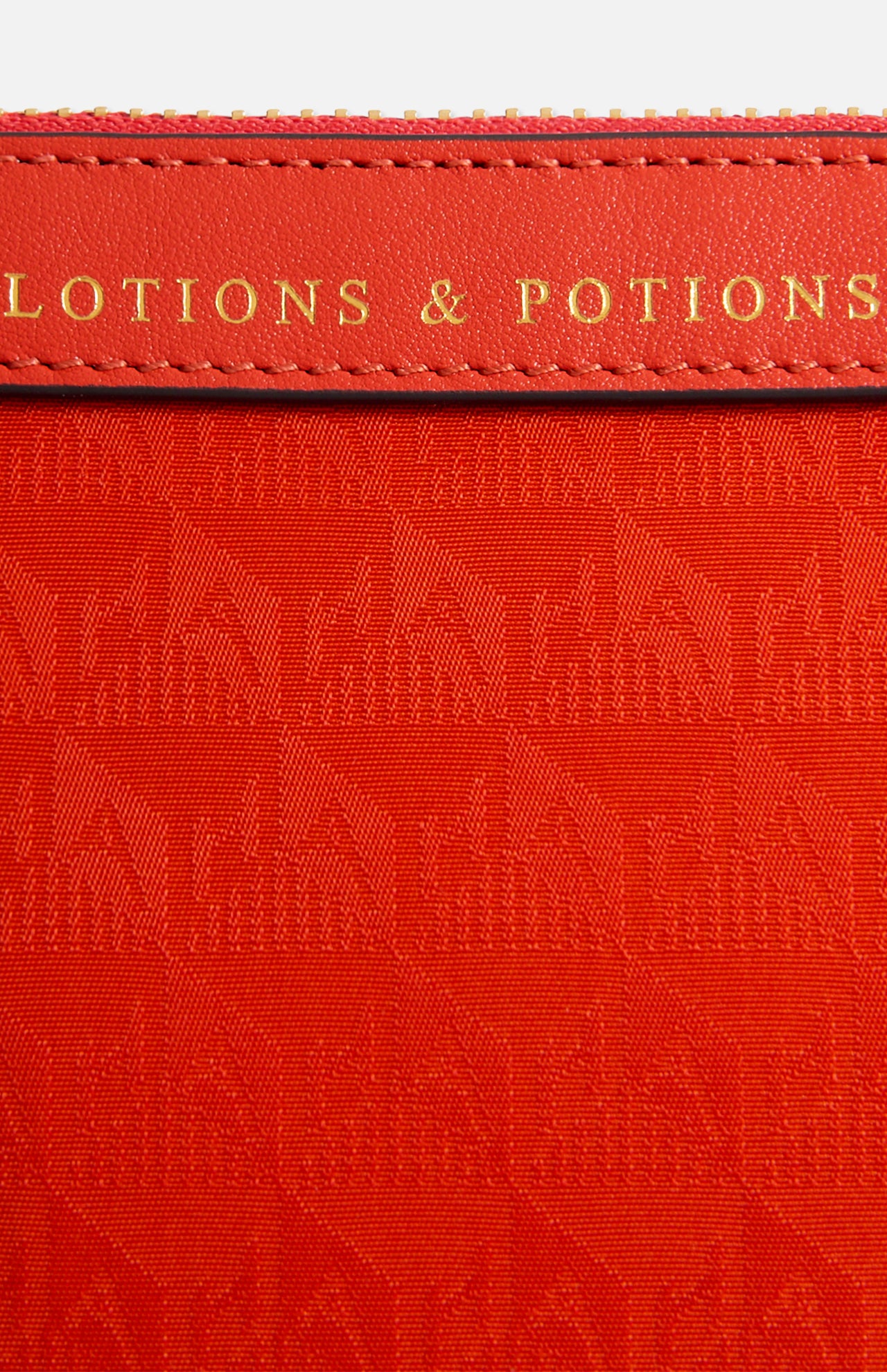 Close-up of a bright orange Anya Hindmarch Lotions and Potions Pouch featuring the embossed text LOTIONS & POTIONS on a leather tab.