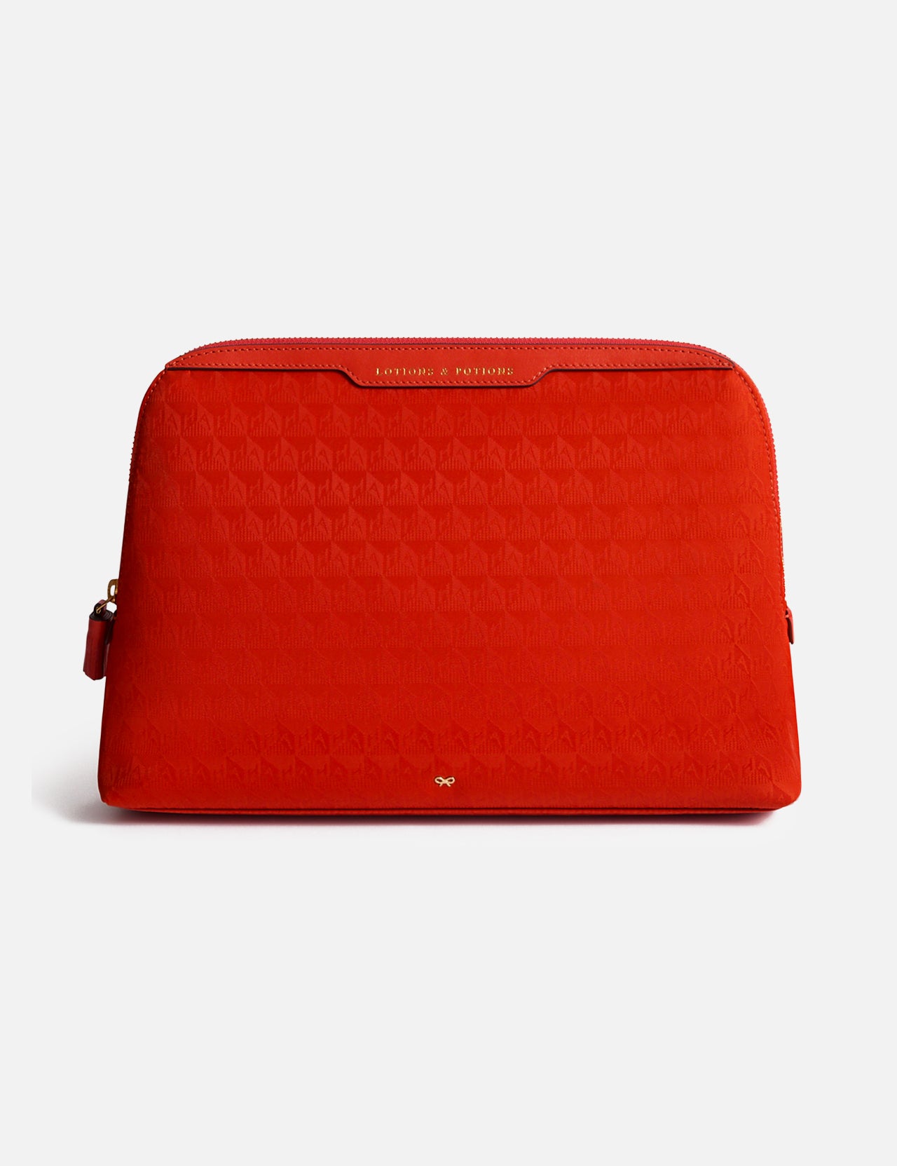 Red zippered Anya Hindmarch Lotions and Potions Pouch featuring a repeating geometric pattern and the words LOTIONS & POTIONS embossed in gold on the top trim.