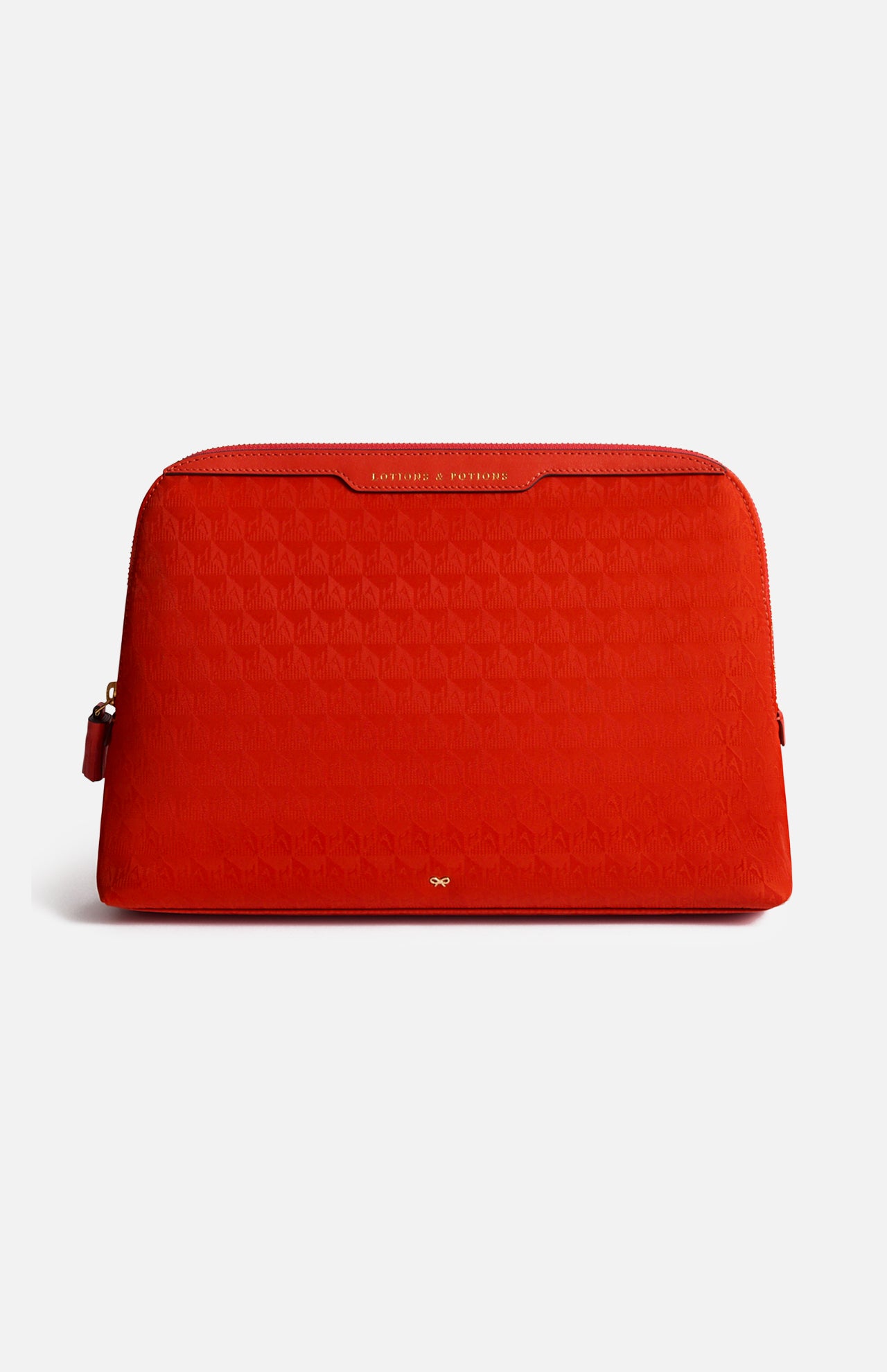 Red zippered Anya Hindmarch Lotions and Potions Pouch featuring a repeating geometric pattern and the words LOTIONS & POTIONS embossed in gold on the top trim.