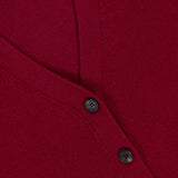Close-up of a deep red v-neck Bleeker Shaped Cashmere Cardigan by ARLO MOTT, featuring black buttons and a visible collar label with the brand’s name. The knit cashmere fabric and classic design highlight the luxurious look, making it an elegant Italian yarn cardigan.
