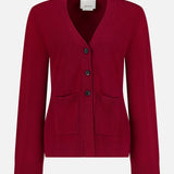 The Bleeker Shaped Cashmere Cardigan by ARLO MOTT is a red V-neck design, expertly knitted from luxurious Italian cashmere. It features long sleeves, three black buttons down the front, and two front pockets. Ribbed detailing at the cuffs and hem adds a refined touch. Presented against a plain white background.