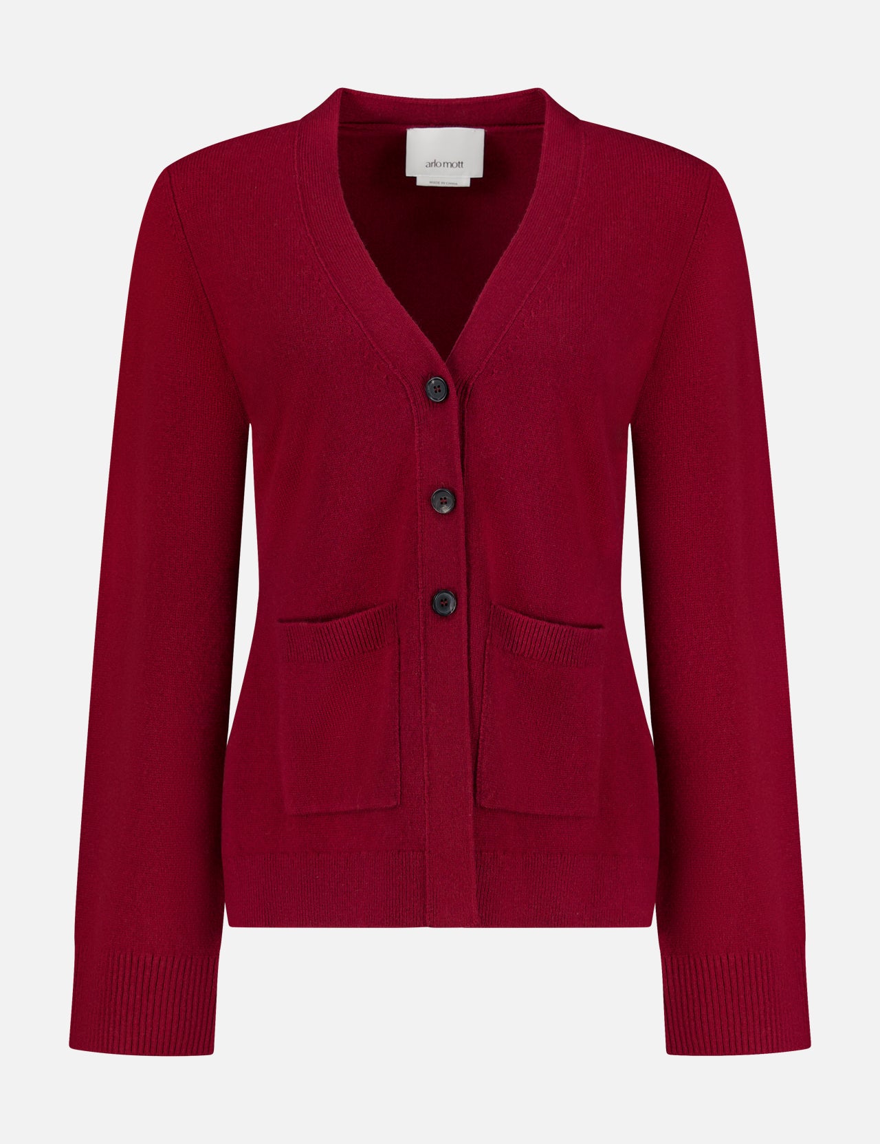 The Bleeker Shaped Cashmere Cardigan by ARLO MOTT is a red V-neck design, expertly knitted from luxurious Italian cashmere. It features long sleeves, three black buttons down the front, and two front pockets. Ribbed detailing at the cuffs and hem adds a refined touch. Presented against a plain white background.