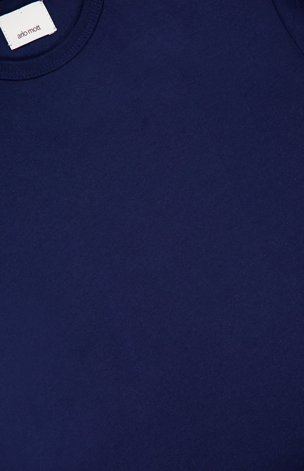 Close-up of the Hubert Short Sleeve Maxi Dress by ARLO MOTT, made from 100% cotton, featuring a plain navy blue design with a round neckline and a white clothing label at the top left.