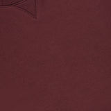 A close-up of the Kent Crewneck with Side Snaps by ARLO MOTT in a berry color, featuring a visible ribbed neckline and a small white clothing label that reads ARLO MOTT and MADE IN THE UK.