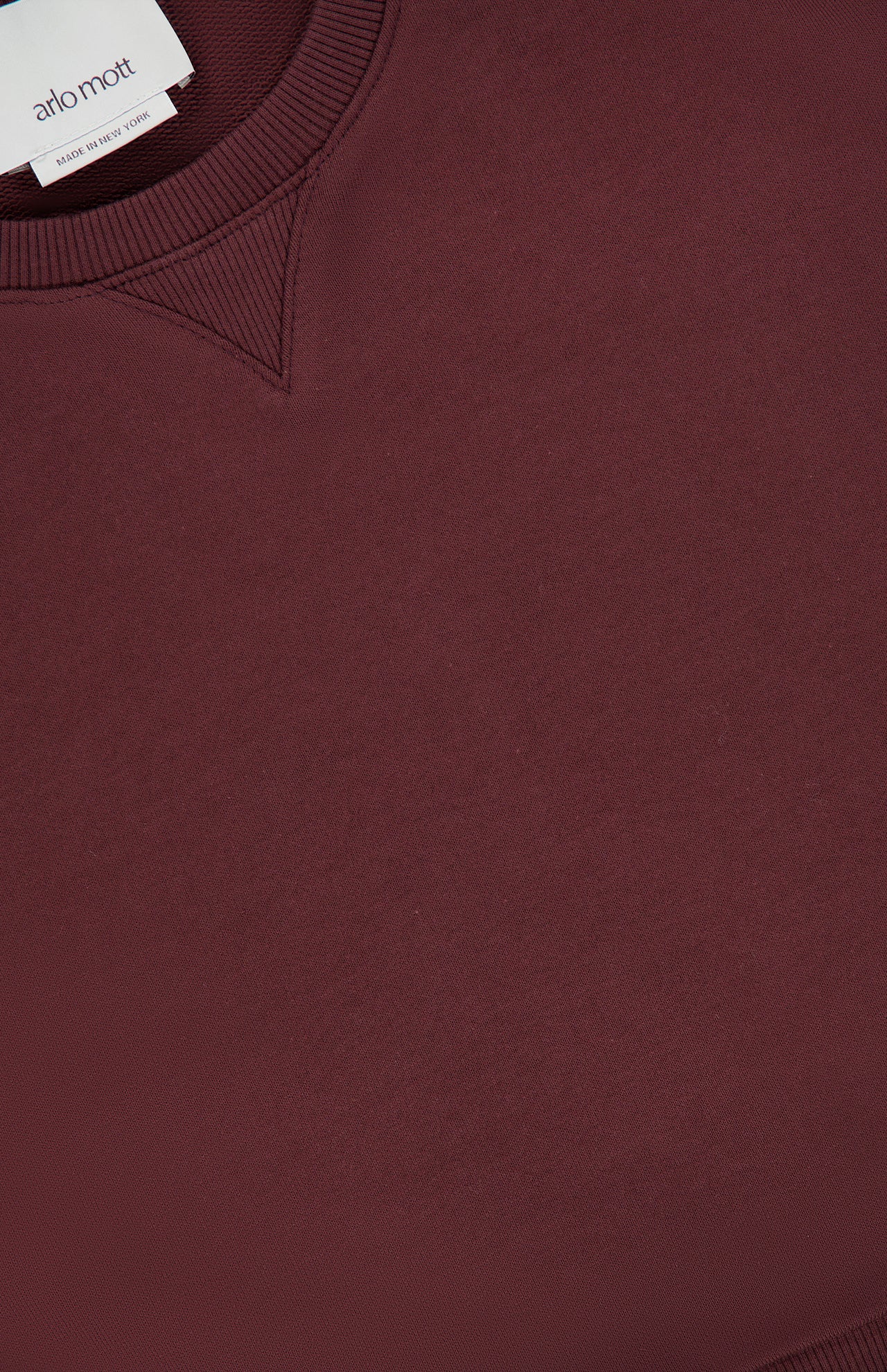 A close-up of the Kent Crewneck with Side Snaps by ARLO MOTT in a berry color, featuring a visible ribbed neckline and a small white clothing label that reads ARLO MOTT and MADE IN THE UK.