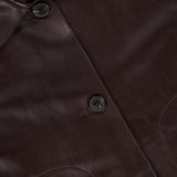 Close-up of the ARMA Emy Lamb Butter Coat, a dark brown jacket crafted from soft lamb leather, featuring three black buttons and a partially visible white ARMA label at the collar, highlighting its tailored silhouette.