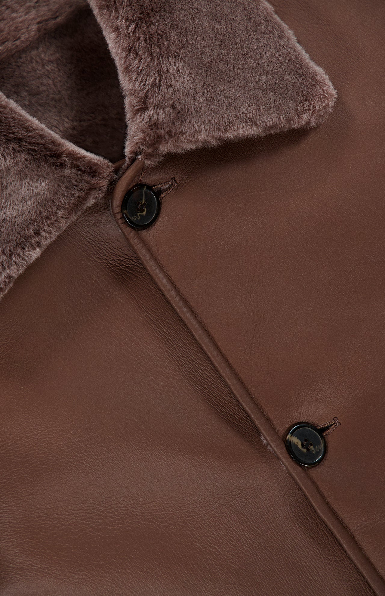 Close-up of the Nicola Reversible Shearling Coat by ARMA, showcasing a soft, textured faux-fur collar and two dark marbled buttons. The smooth matte finish contrasts with the plush, warm-toned collar.