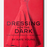 ASSOULINE’s “Dressing For The Dark” book cover showcases a red strapless evening gown set against a matching red background, with bold black lettering—a striking nod to memorable moments in fashion.