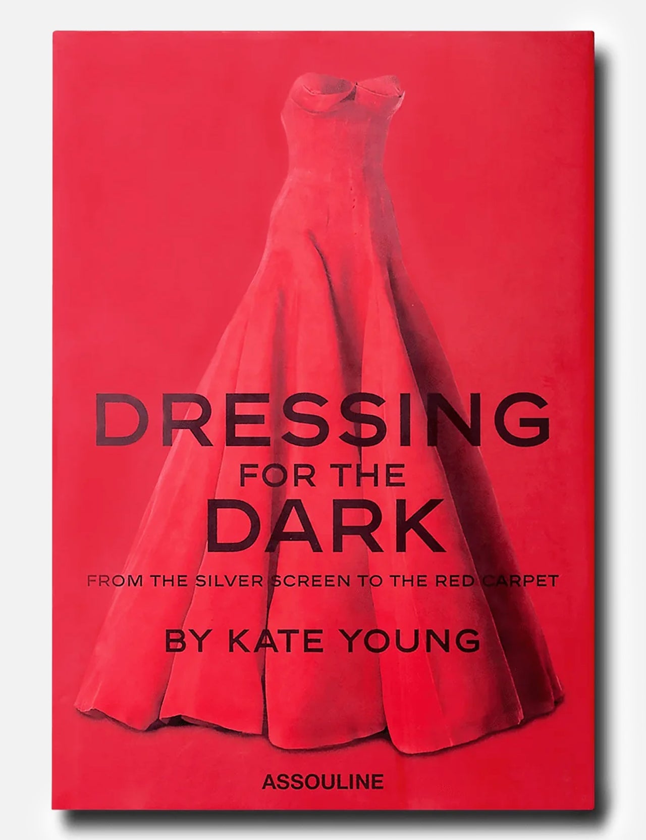 ASSOULINE’s “Dressing For The Dark” book cover showcases a red strapless evening gown set against a matching red background, with bold black lettering—a striking nod to memorable moments in fashion.