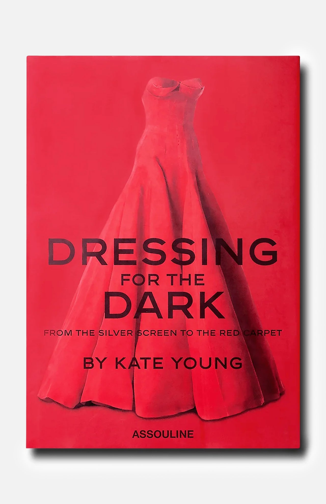 ASSOULINE’s “Dressing For The Dark” book cover showcases a red strapless evening gown set against a matching red background, with bold black lettering—a striking nod to memorable moments in fashion.