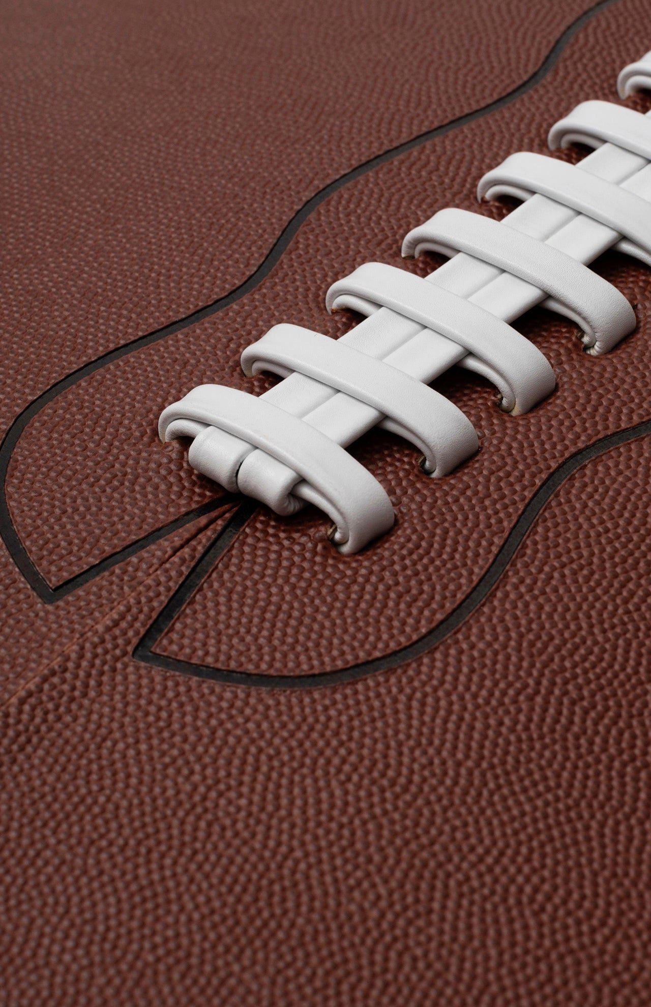 Close-up of a textured brown American football with white laces and stitched seam, as featured in ASSOULINE’s "Football: The Impossible Collection," celebrating iconic moments in NFL and college football history.