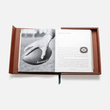 An open brown case from ASSOULINE's "Football: The Impossible Collection" shows a black-and-white photo of a hand holding a football on the left and a printed college football introduction with a small football illustration on the right.