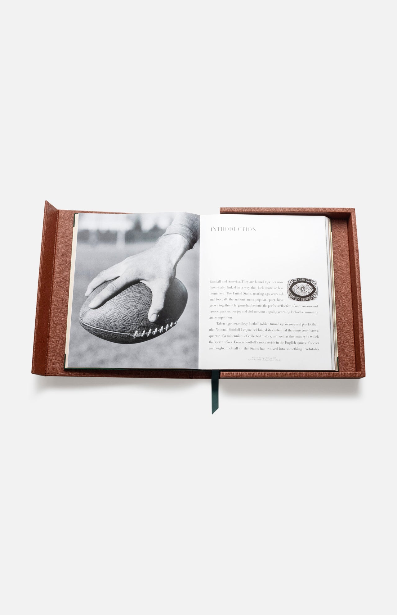 An open brown case from ASSOULINE's "Football: The Impossible Collection" shows a black-and-white photo of a hand holding a football on the left and a printed college football introduction with a small football illustration on the right.