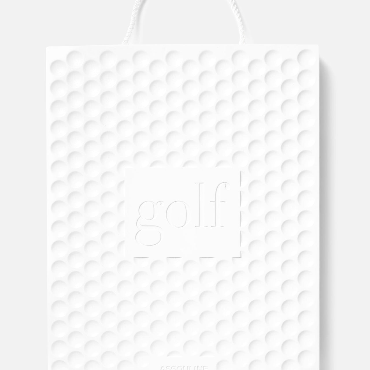 A white textured shopping bag with a golf ball pattern, rope handle, and “golf” embossed on the front celebrates ASSOULINE’s Golf: The Impossible Collection and showcases famous golf courses with the ASSOULINE brand at the bottom.