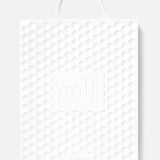 A white textured shopping bag with a golf ball pattern, rope handle, and “golf” embossed on the front celebrates ASSOULINE’s Golf: The Impossible Collection and showcases famous golf courses with the ASSOULINE brand at the bottom.